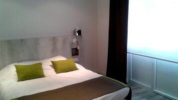 Una cama bien hecha con una colcha blanca y marrón, dos almohadas verdes y una mesita de noche con una lámpara.