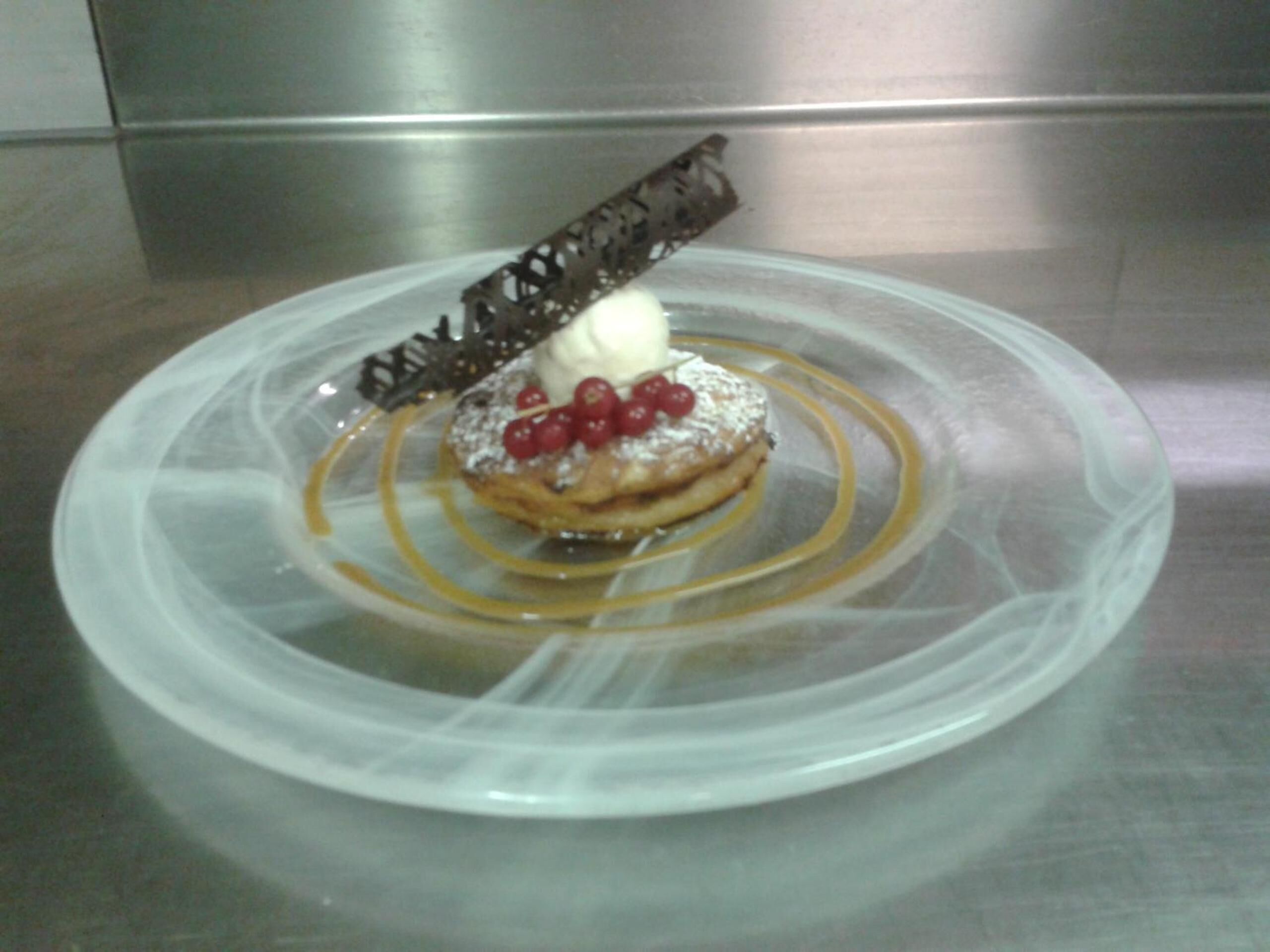 A dessert on a clear plastic plate with a caramel drizzle and a chocolate decoration.