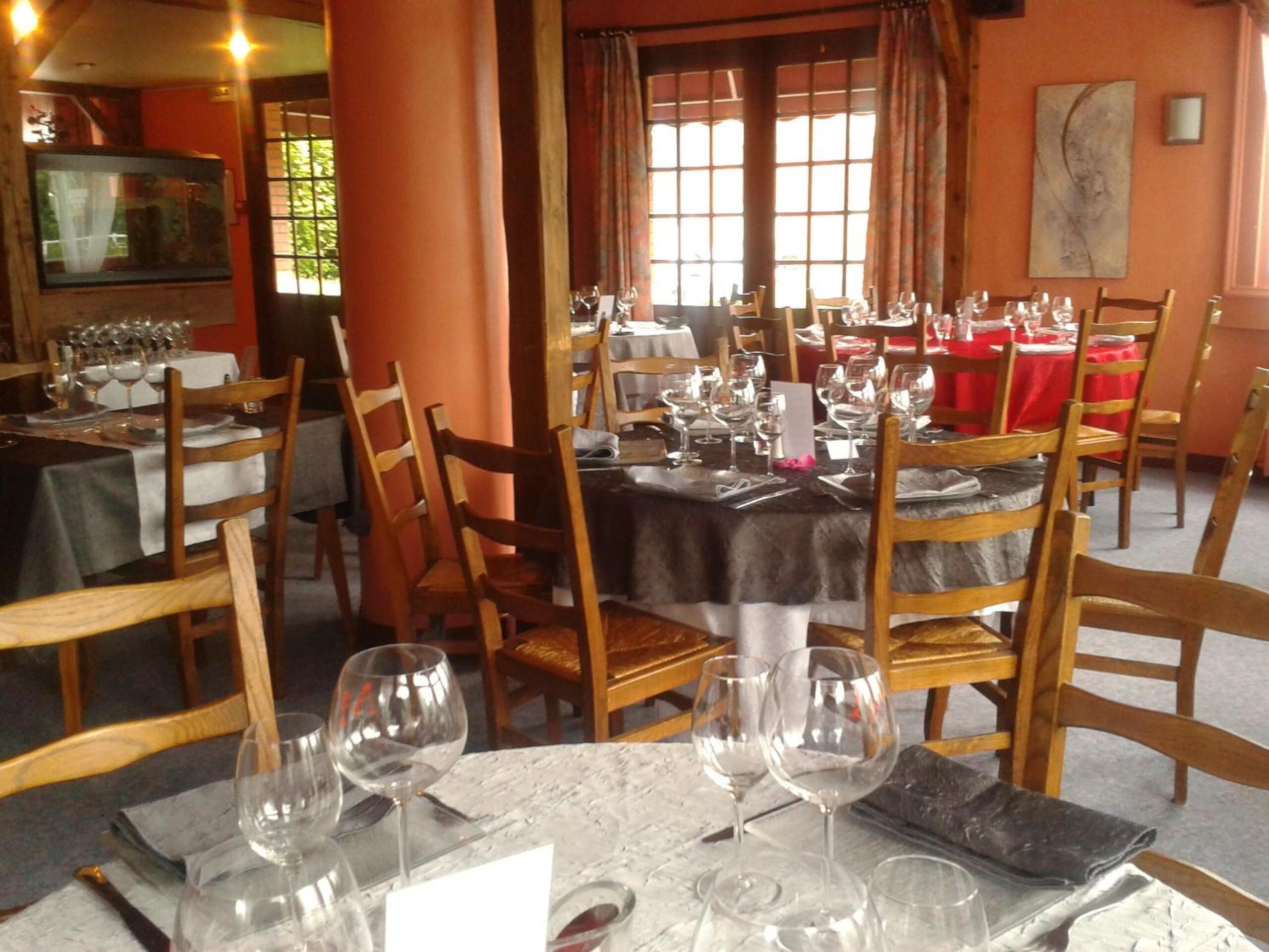 A restaurant with tables set for dining, wooden chairs, and a large window with curtains.