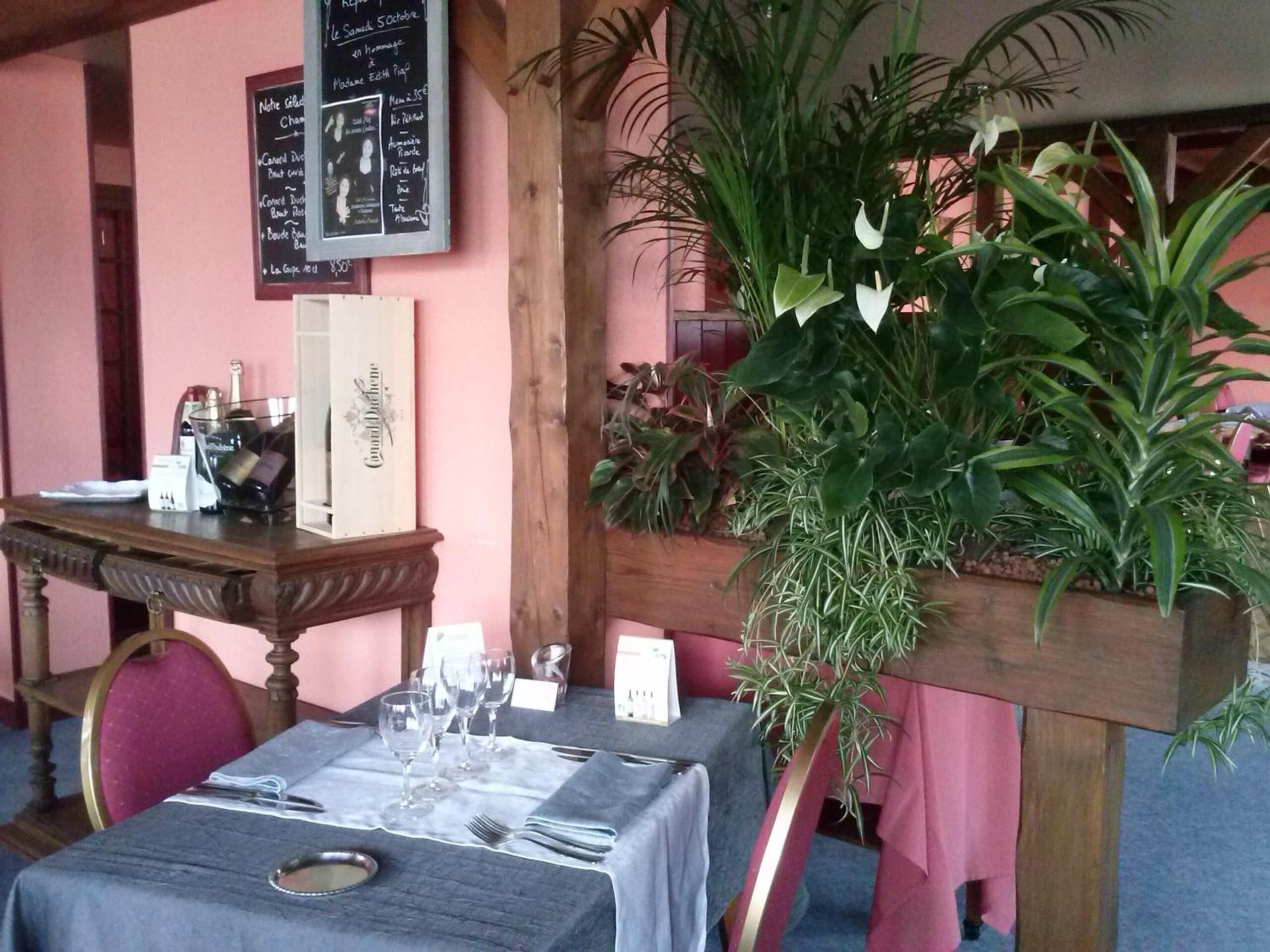 Interior de un restaurante con una mesa lista para comer, un tablero de menú y diversas plantas.