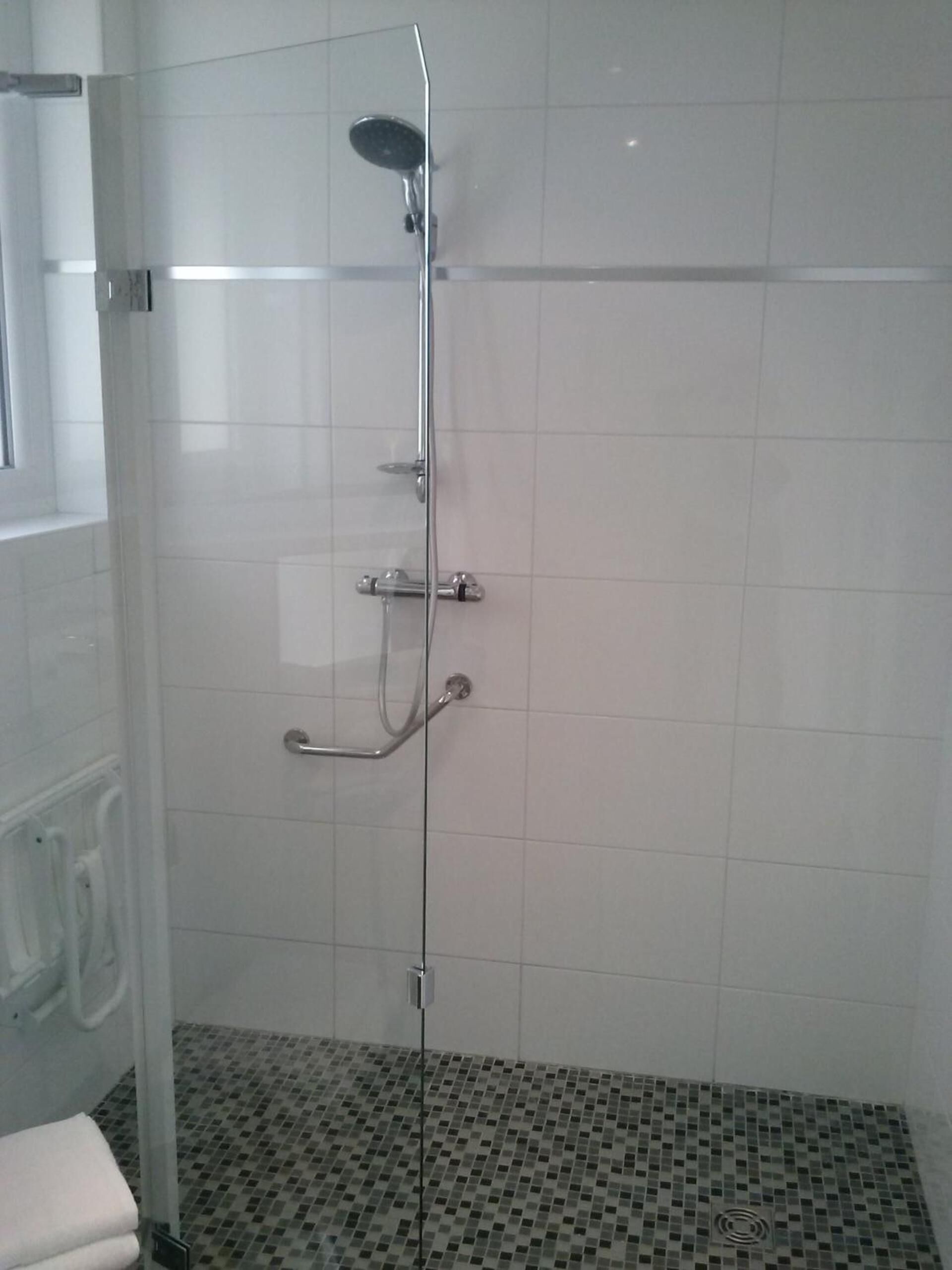 Eine Dusche mit Glastür, Duschbrause und fest installierter Bedienung.