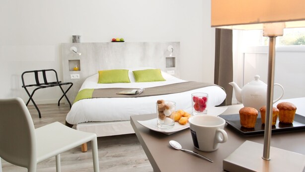 Une chambre d’hôtel moderne équipée d’un lit, d’une table à manger avec des articles pour le petit-déjeuner, d’une chaise et d’une lampe.