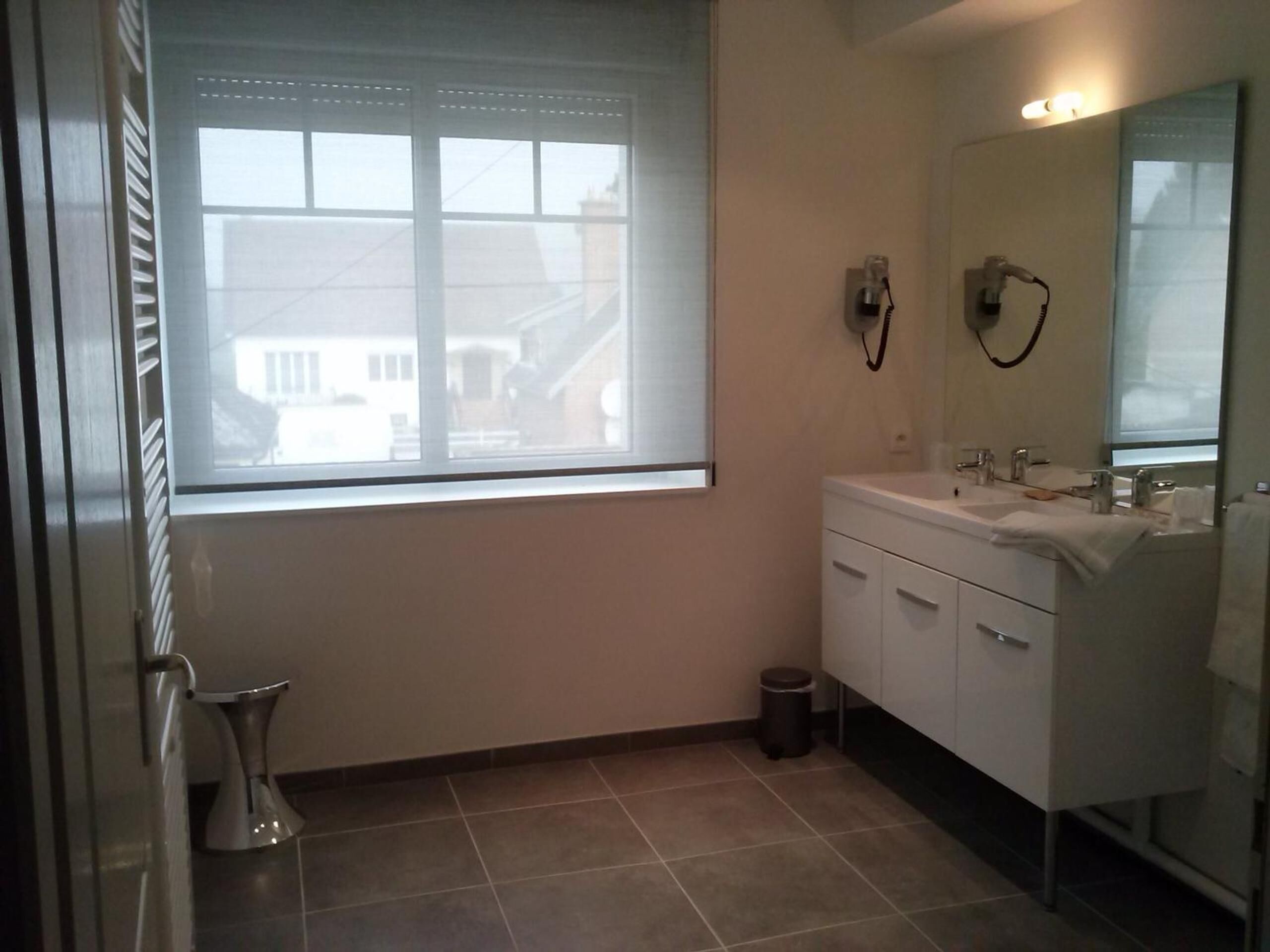 Ein Badezimmer mit Fenster, Waschbecken, Spiegel und Mülleimer.