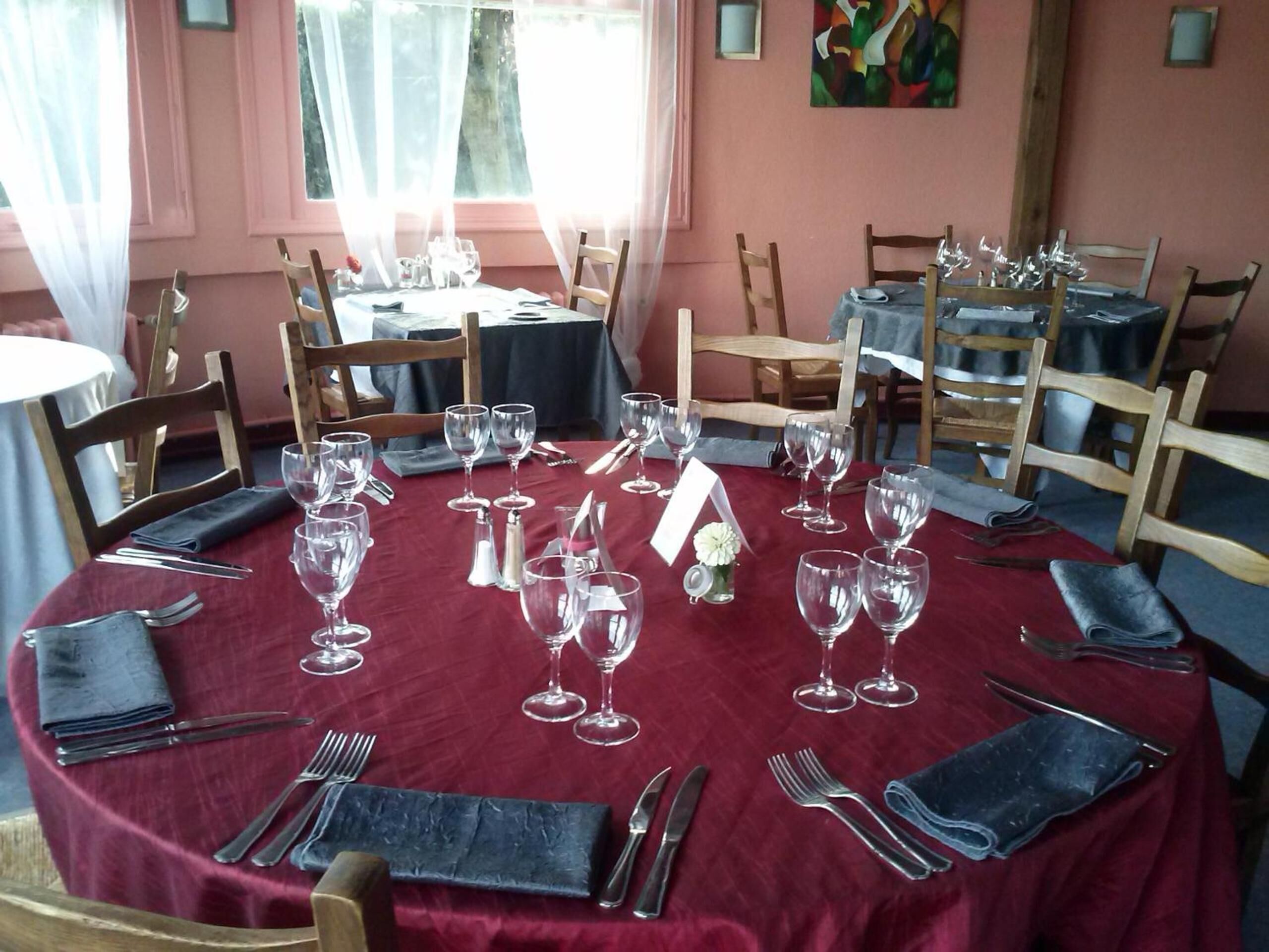 A dining area with round tables set for a meal, each with a red tablecloth, silverware, and wine glasses.