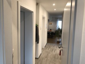 A narrow hallway with white walls and a wooden floor, leading to a dining area with a table and chairs. - Ferienwohnungen Scheuring (Volkach)
