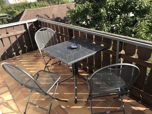 An outdoor patio with a metal table and two chairs, surrounded by a wooden fence and a tiled floor. - Ferienwohnungen Scheuring (Volkach)