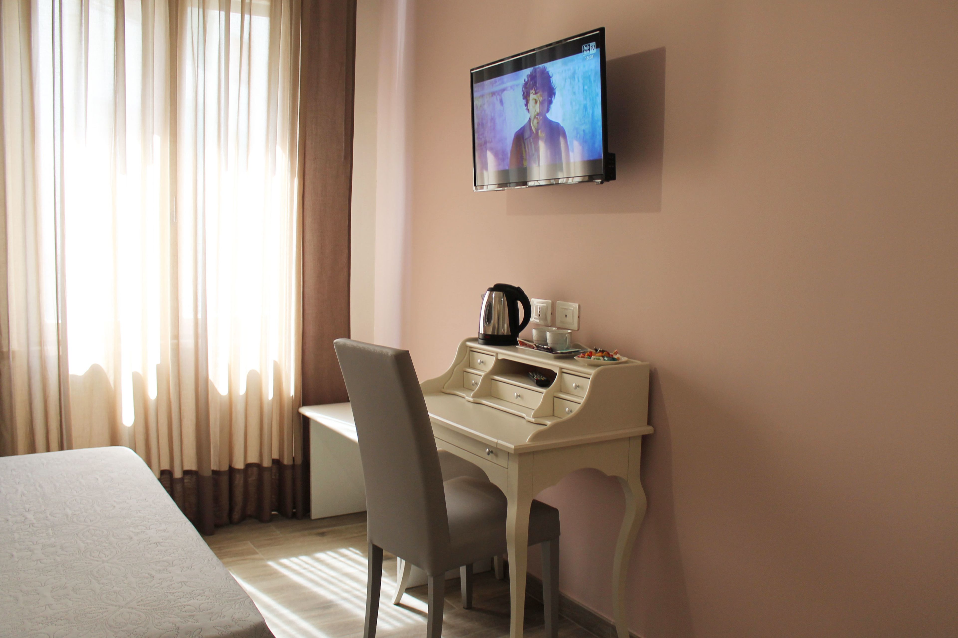 A hotel room with a bed, a desk with a chair, a television mounted on the wall, and a window with curtains.