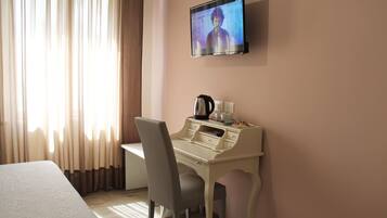 A hotel room with a bed, a desk with a chair, a television mounted on the wall, and a window with curtains.