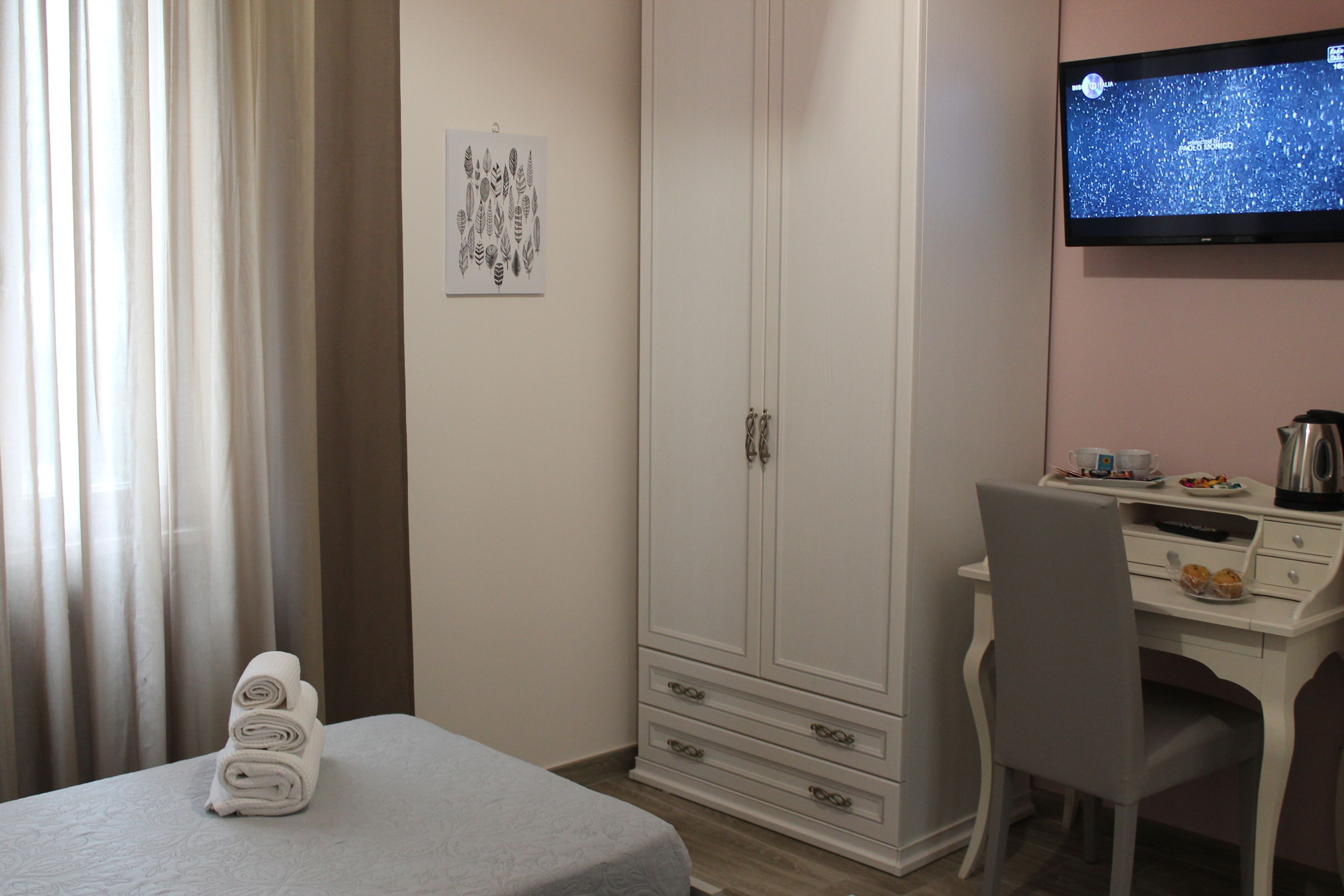Una camera d'albergo con un letto, una scrivania con una sedia, un armadio e un televisore appeso al muro.