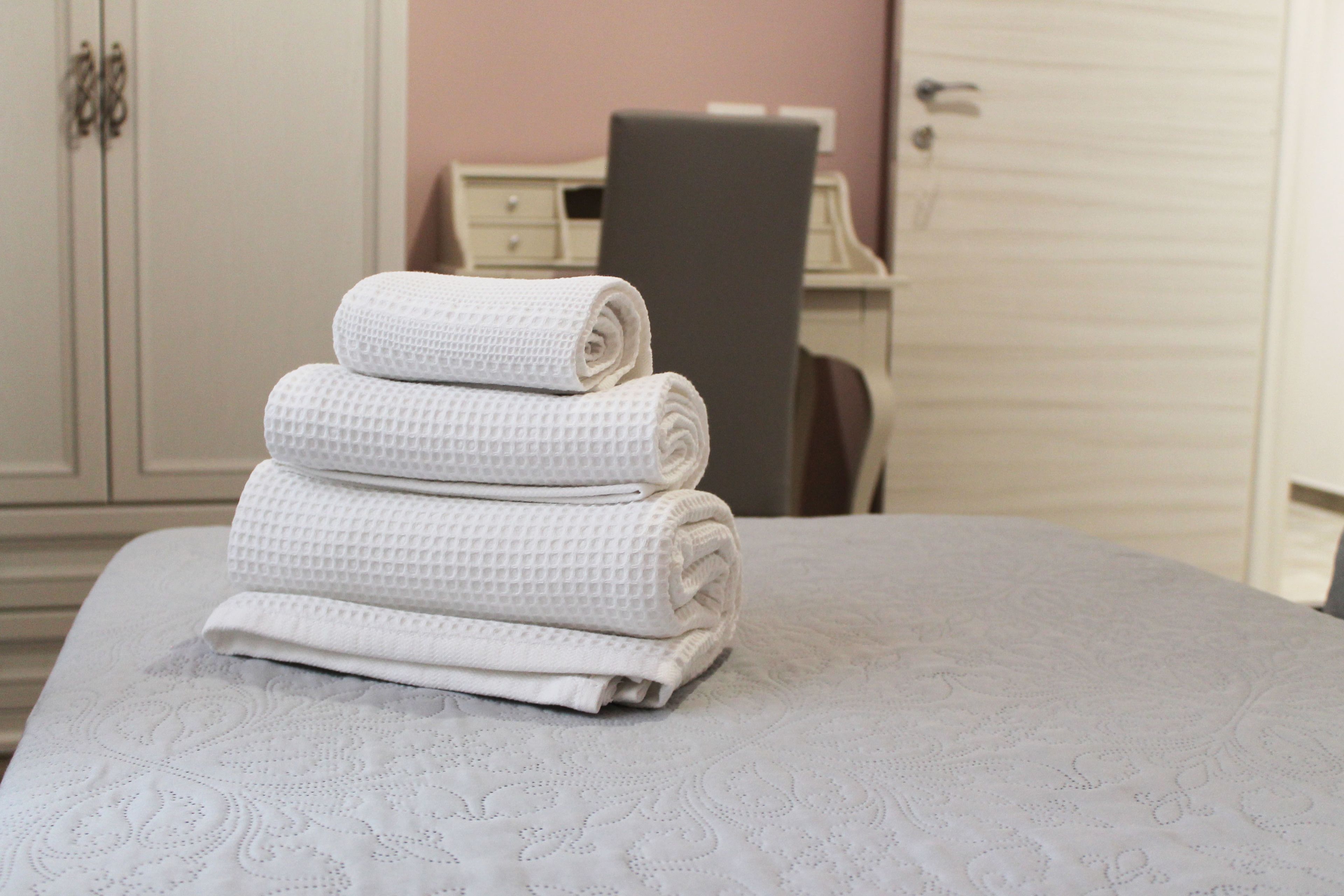 Una cama bien hecha con una colcha blanca texturizada y toallas blancas enrolladas apiladas encima.