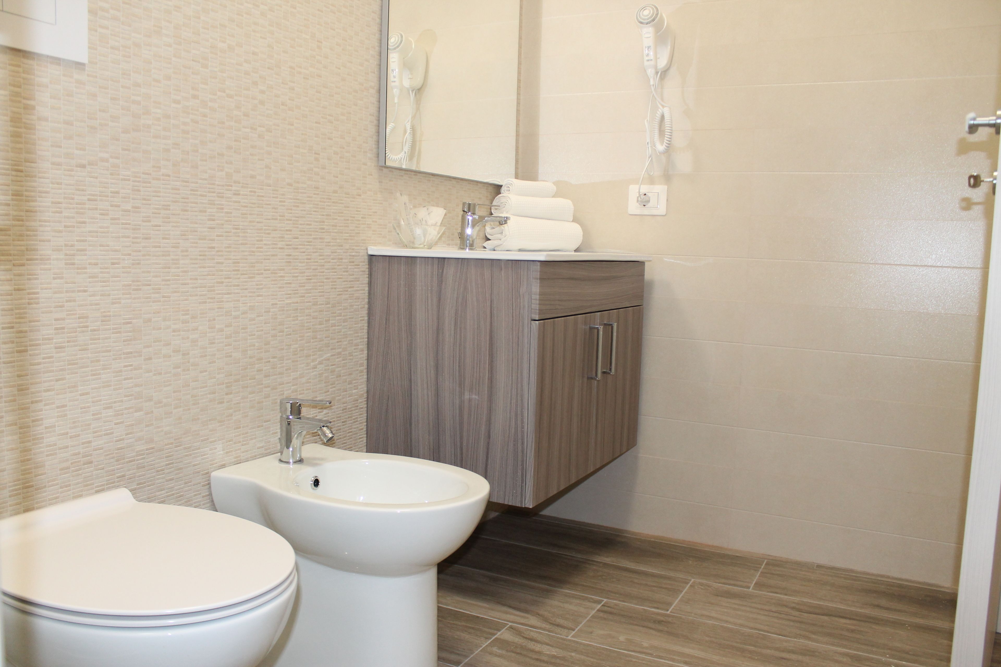 Une salle de bain moderne comprenant des toilettes, un bidet, un meuble-lavabo avec un miroir et un porte-serviettes.
