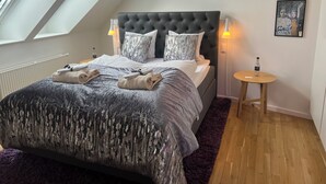 A modern bedroom with a large bed, a skylight, a round wooden side table, and artwork on the wall. - Mortens Kro Boutique Hotel (Aalborg)