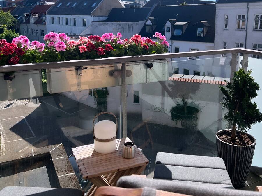 A rooftop terrace with a wooden table, a potted plant, and a chair.