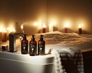 A bathroom with a bathtub, three bottles of Mortens Kro shower gel, and candles. - Mortens Kro Boutique Hotel (Aalborg)