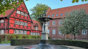 A courtyard with a fountain, surrounded by a hedge and a red building with white window frames. - Mortens Kro Boutique Hotel (Aalborg)