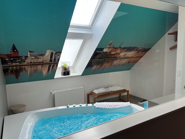 Un baño moderno con una bañera grande, un tragaluz y un mural con vistas a la ciudad.