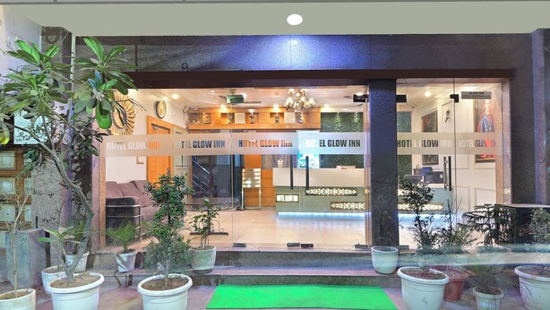 La entrada del Hotel Glow Inn con un cartel sobre la puerta, plantas en macetas al frente y un mostrador de recepción en el interior.