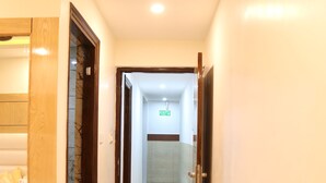 Un pasillo de hotel con una puerta de madera a la izquierda, una puerta de vidrio en el centro y otra puerta de madera a la derecha.
