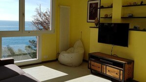 A living room with a large window, a beige bean bag chair, a TV, and a wooden cabinet. - Lovely Apartment on the Ligurian Sea (Varazze)