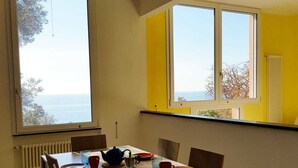 A dining area with a table set for four, two windows with views of the sea, and a radiator on the wall. - Lovely Apartment on the Ligurian Sea (Varazze)