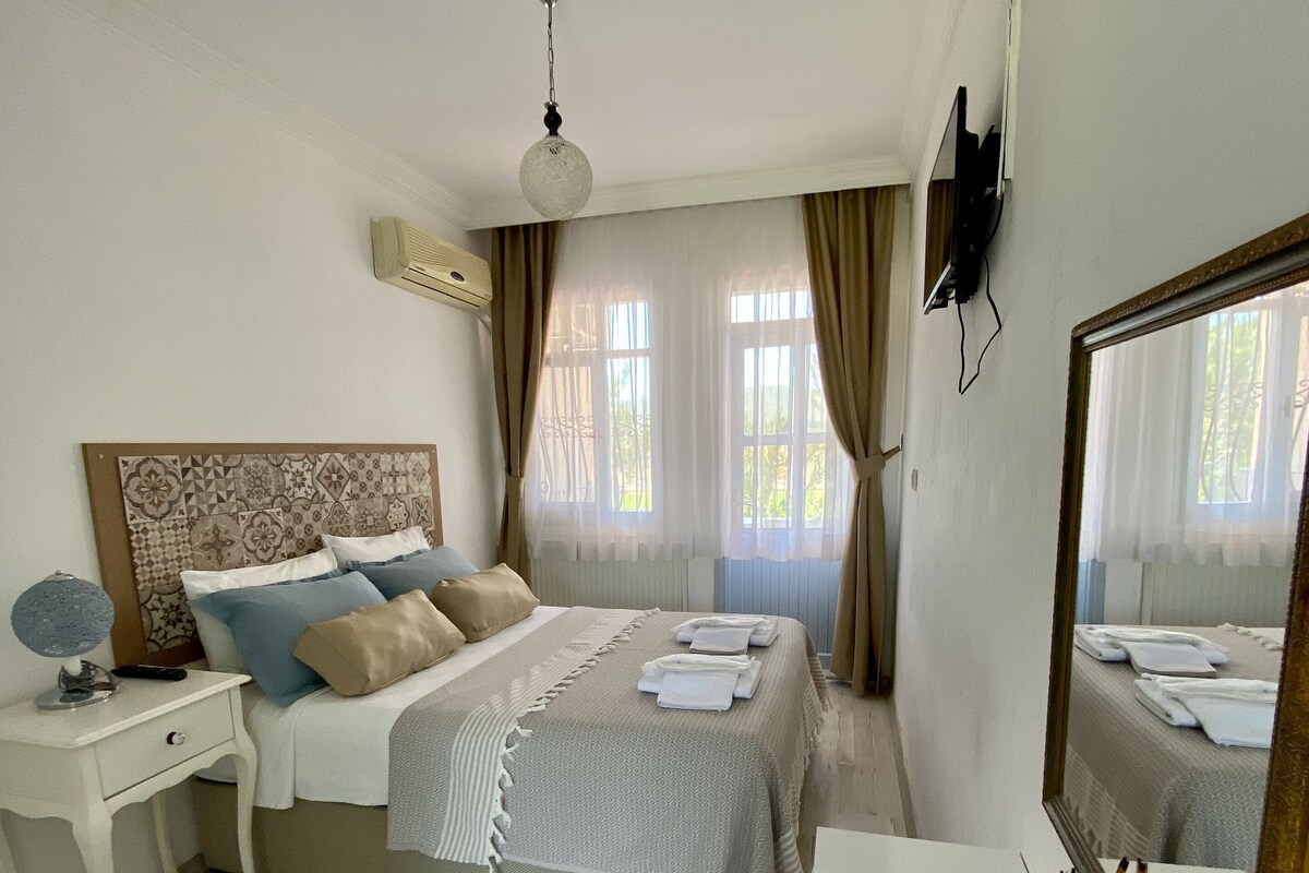 Une chambre à coucher avec un lit, une table de chevet, un miroir et une fenêtre avec des rideaux.