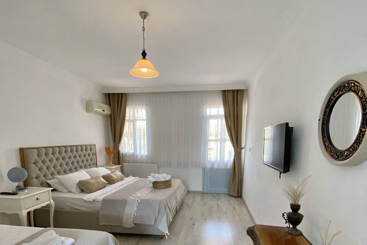 Una habitación de hotel con una cama, mesitas de noche, un televisor, un espejo y una mesa de madera.