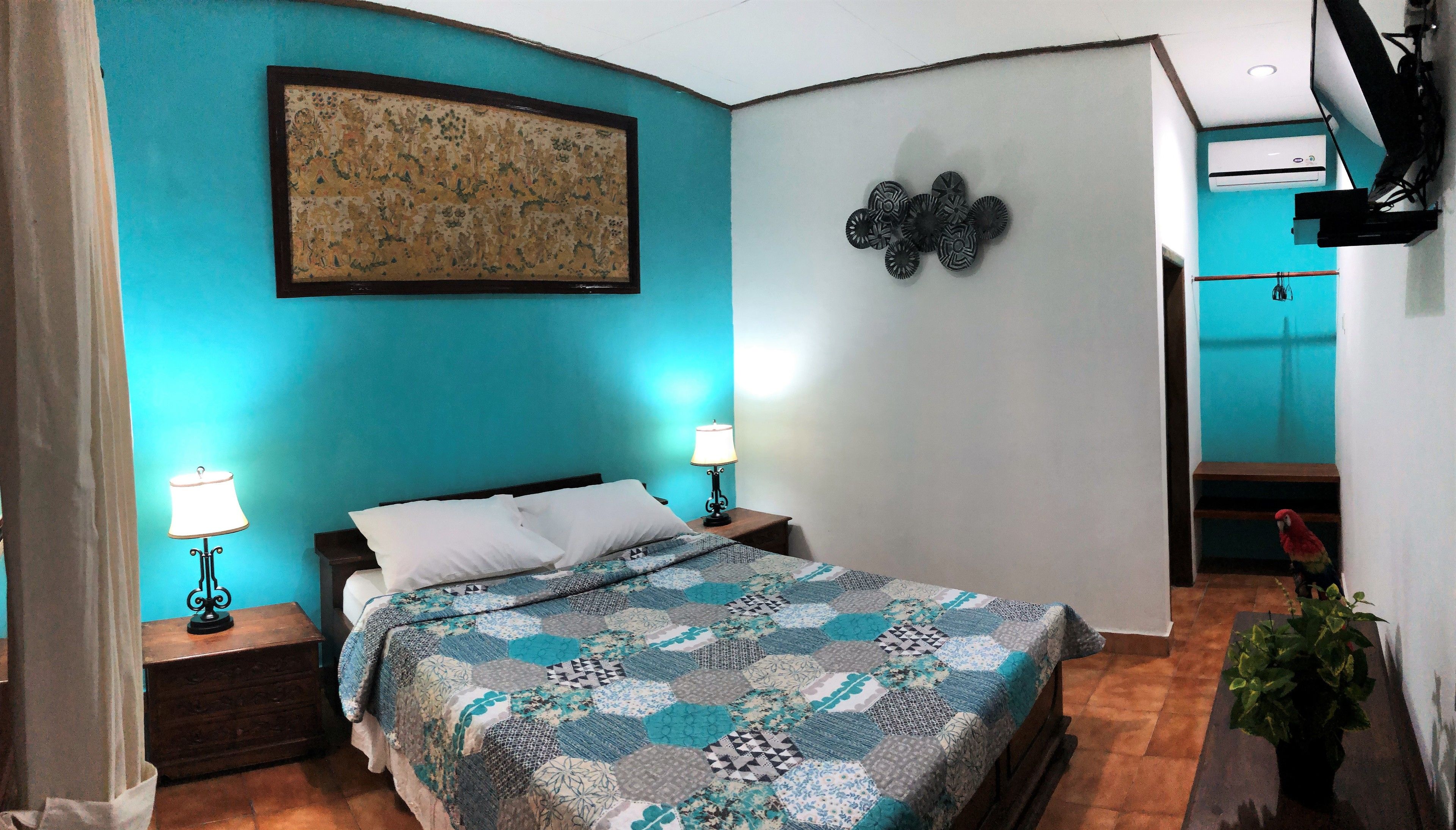 Um quarto com uma cama, duas mesas de cabeceira com abajures, uma obra de arte na parede e um enfeite de parede.