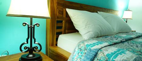 Una cama bien hecha con un edredón estampado, un cabecero de madera y dos lámparas de noche.