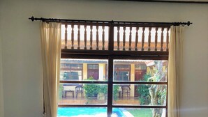 A room with a sofa, a small table with a plant, and a window with curtains. - Mangga Bungalow (Denpasar)