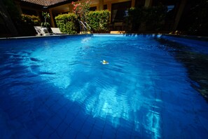 A swimming pool with clear blue water, surrounded by lounge chairs and greenery. - Mangga Bungalow (Denpasar)