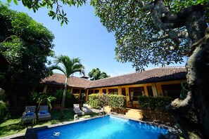 A pool area with lounge chairs and a building with a tiled roof. - Mangga Bungalow (Denpasar)