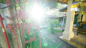 A gated entrance with a wrought iron gate, a paved pathway, and a building with a tiled roof. - Mangga Bungalow (Denpasar)