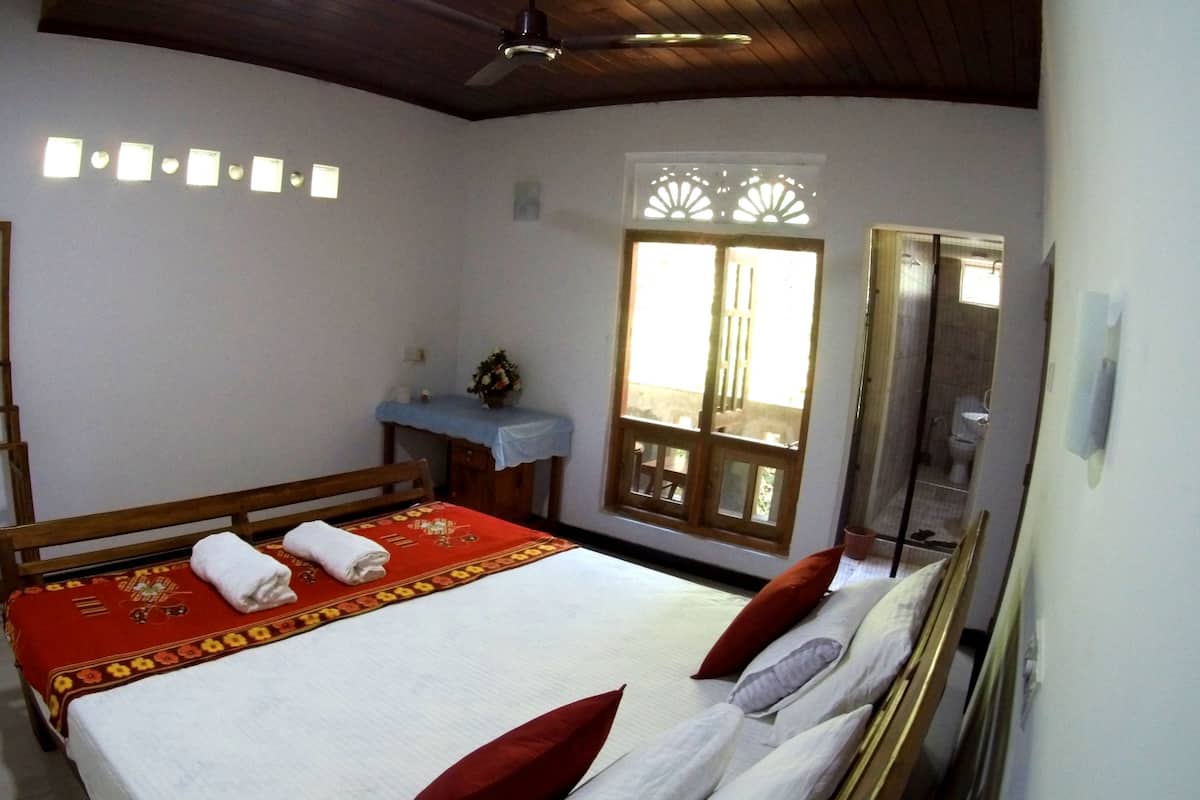 A bedroom with a bed, a desk, a chair, a wardrobe, a window, and a ceiling fan.