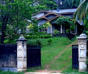 A gated entrance with a pathway leading to a house surrounded by lush greenery.