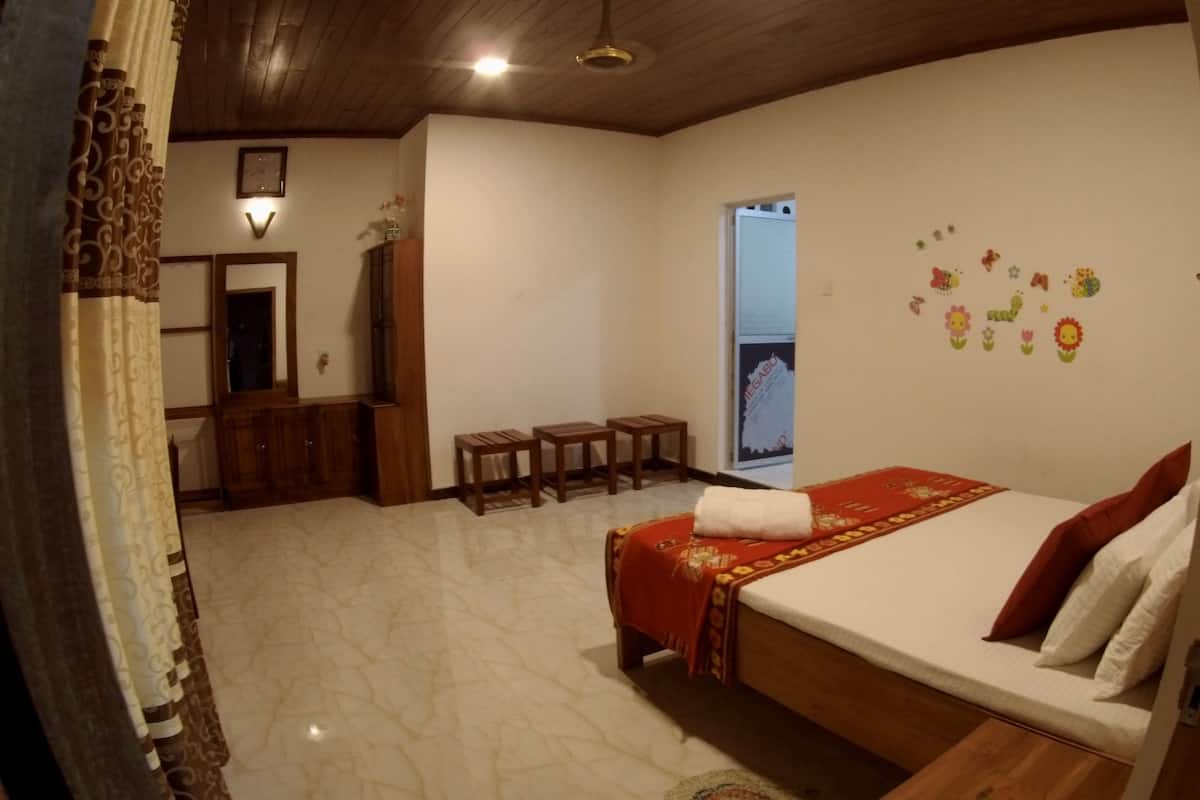 A bedroom with a bed, a wooden wardrobe, a mirror, a small table, and a window with a view.