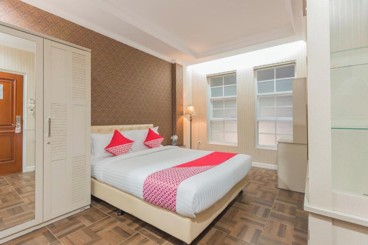 A bedroom with a bed, wardrobe, bedside lamp, and a window.