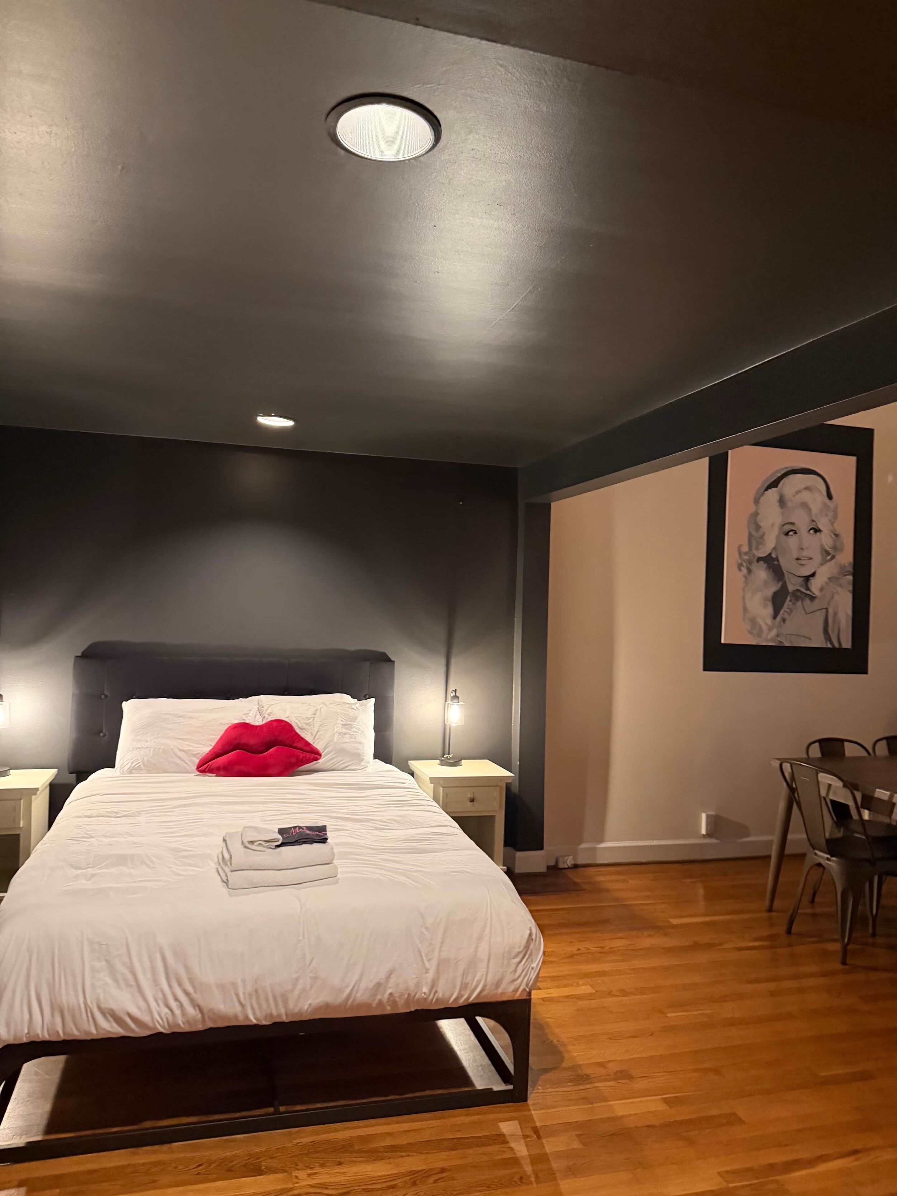 A bedroom with a bed, a nightstand, a chair, and a framed picture on the wall.