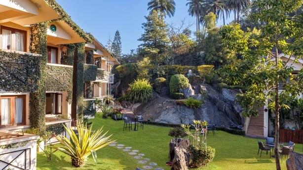 Un patio de hotel con piscina, mobiliario exterior y exuberante jardinería.
