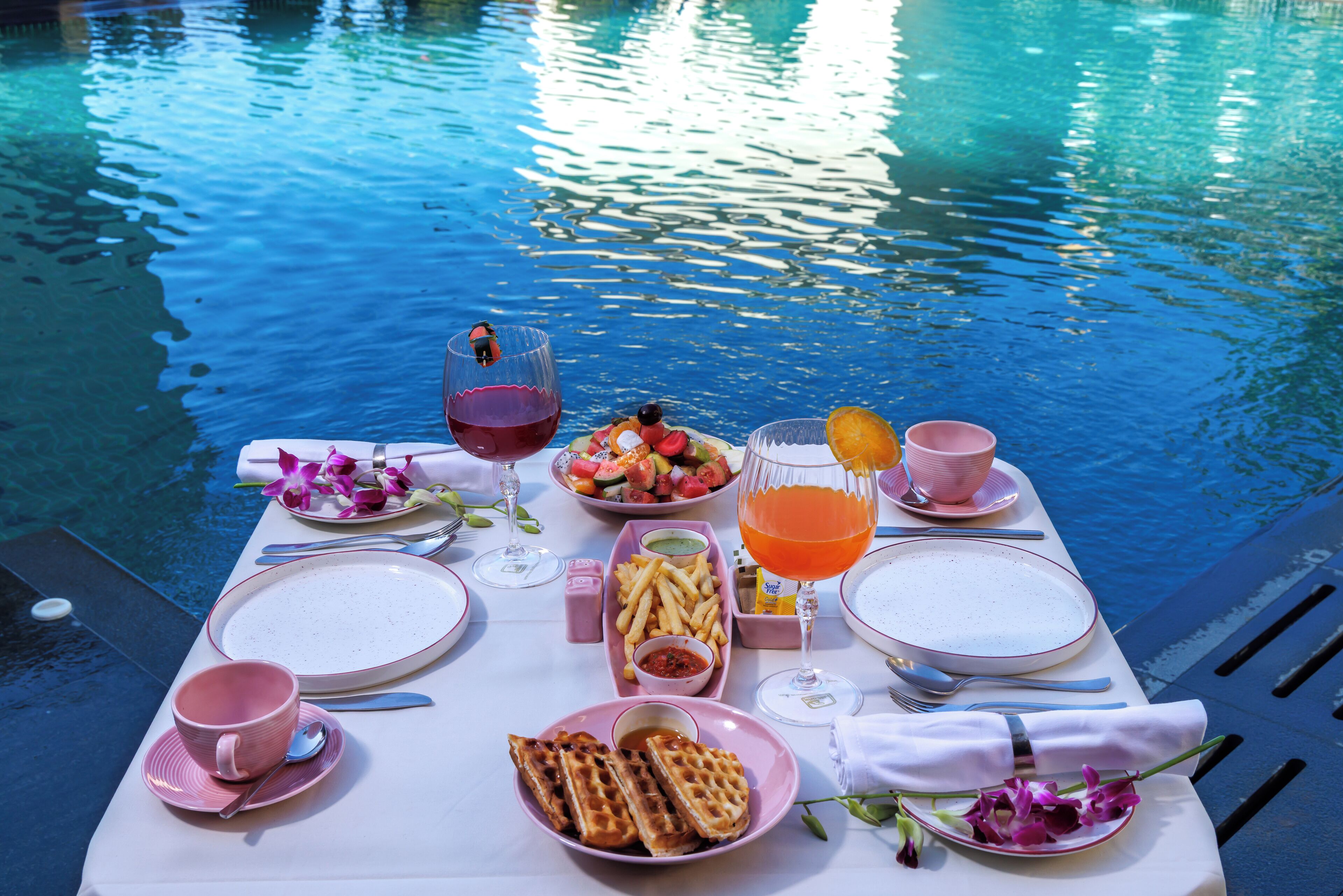 A table set by a pool with plates, cutlery, and a drink.