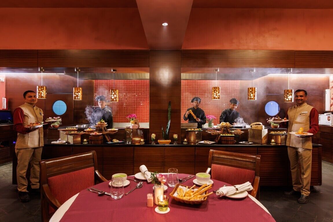 A restaurant with a central dining table set for four, surrounded by staff serving dishes.