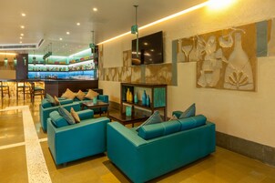 Un vestíbulo con sofás color turquesa, una zona de bar y un televisor montado en la pared.