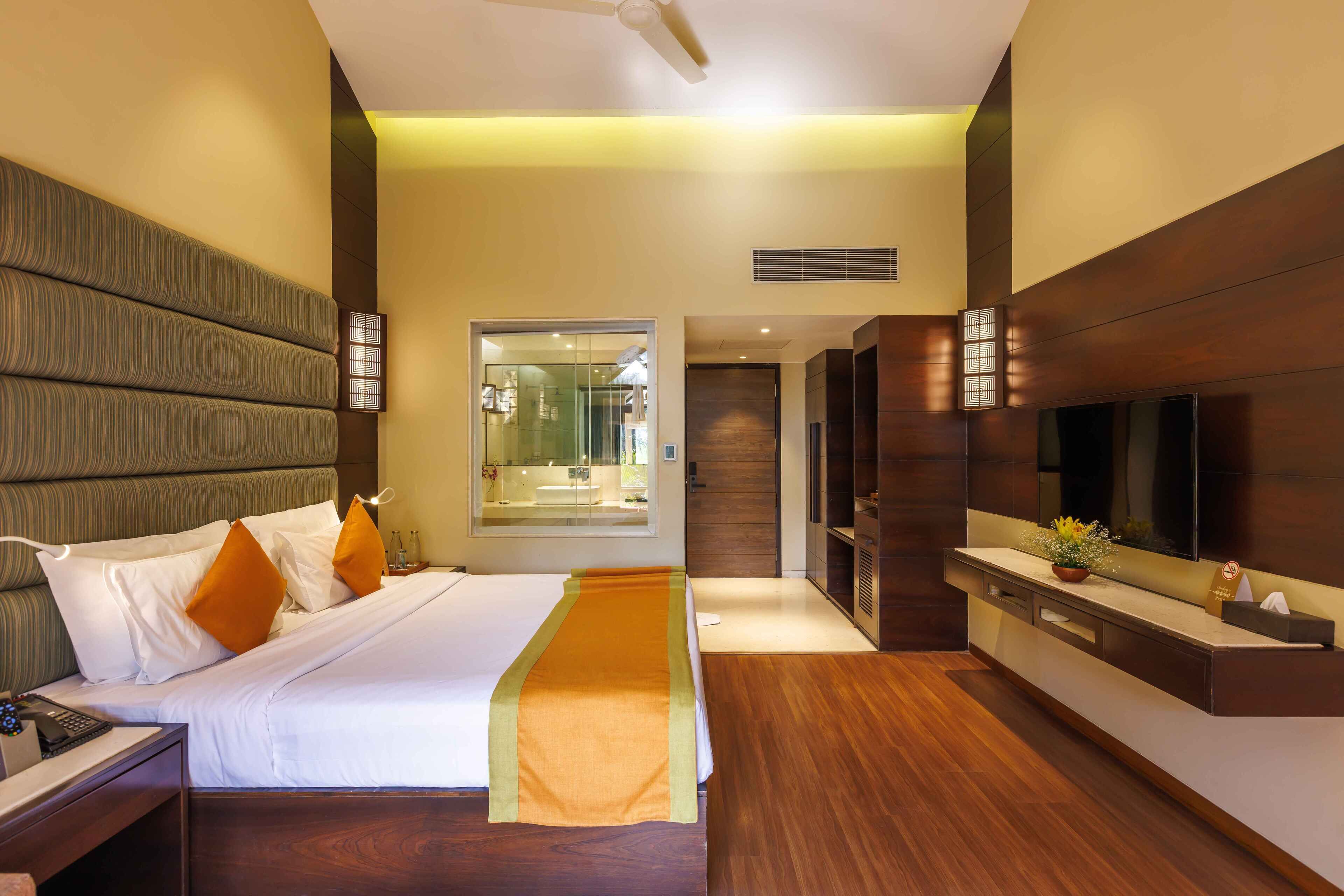 Een moderne hotelkamer met een groot bed, een nachtkastje, een televisie en een badkamer zichtbaar door een glazen deur.