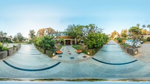 Una entrada de hotel moderna con un camino curvo, asientos al aire libre y un exuberante paisaje.