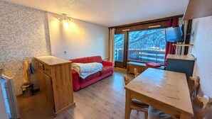 A cozy room with a wooden table, a red sofa, and a large window offering a view of a snowy landscape. - Cozy studio 4 pers, pets allowed, parking, near slopes (Montgenèvre)