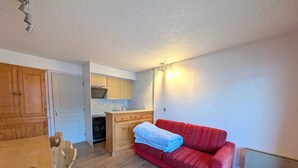 A compact living space with a kitchenette, a red sofa, and a wooden dining table. - Cozy studio 4 pers, pets allowed, parking, near slopes (Montgenèvre)