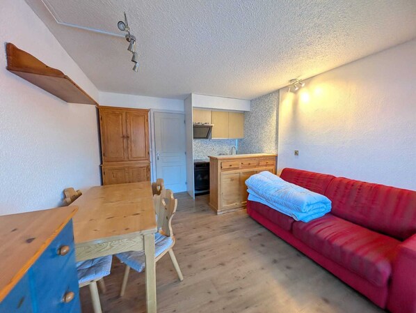 A compact living space with a wooden dining table, a red sofa, a kitchenette, and a small bathroom.