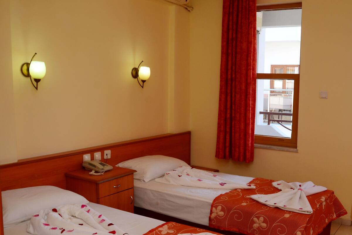 A hotel room with two beds, a nightstand, a telephone, and a window with a red curtain.