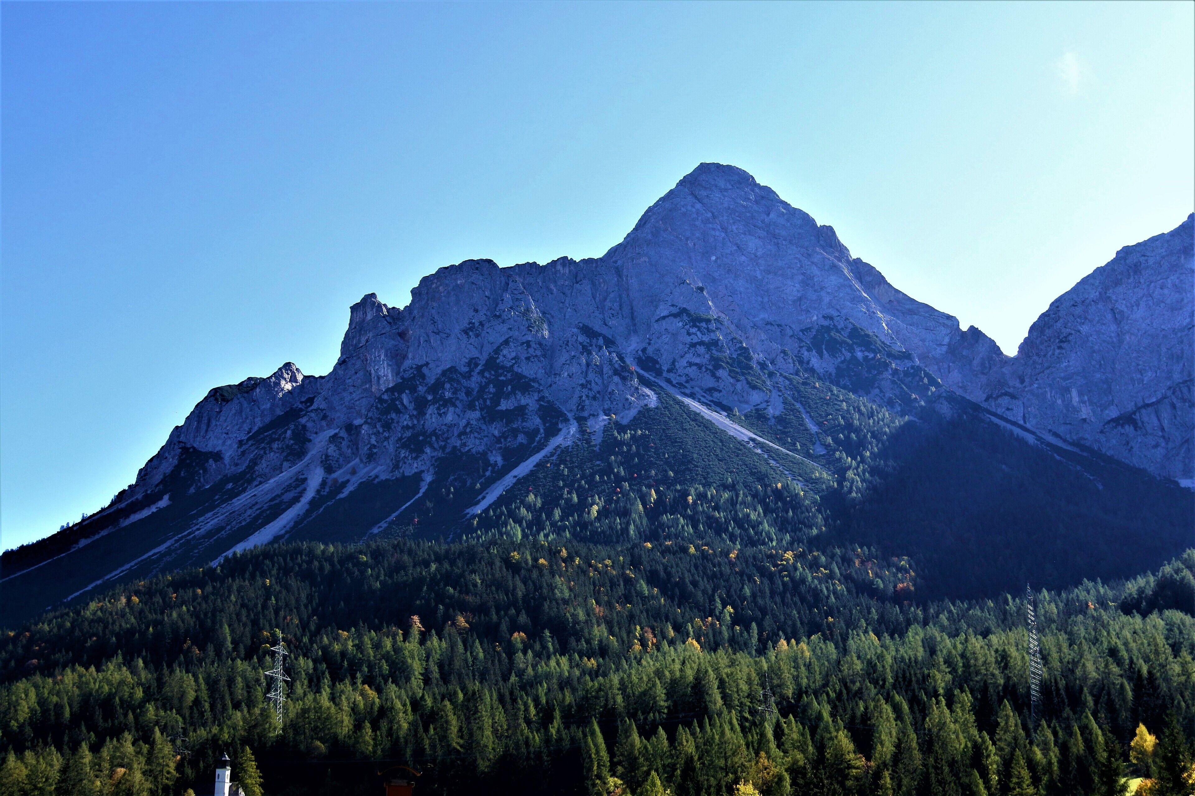A mountain landscape with a prominent peak, dense forest at the base, and a clear sky.