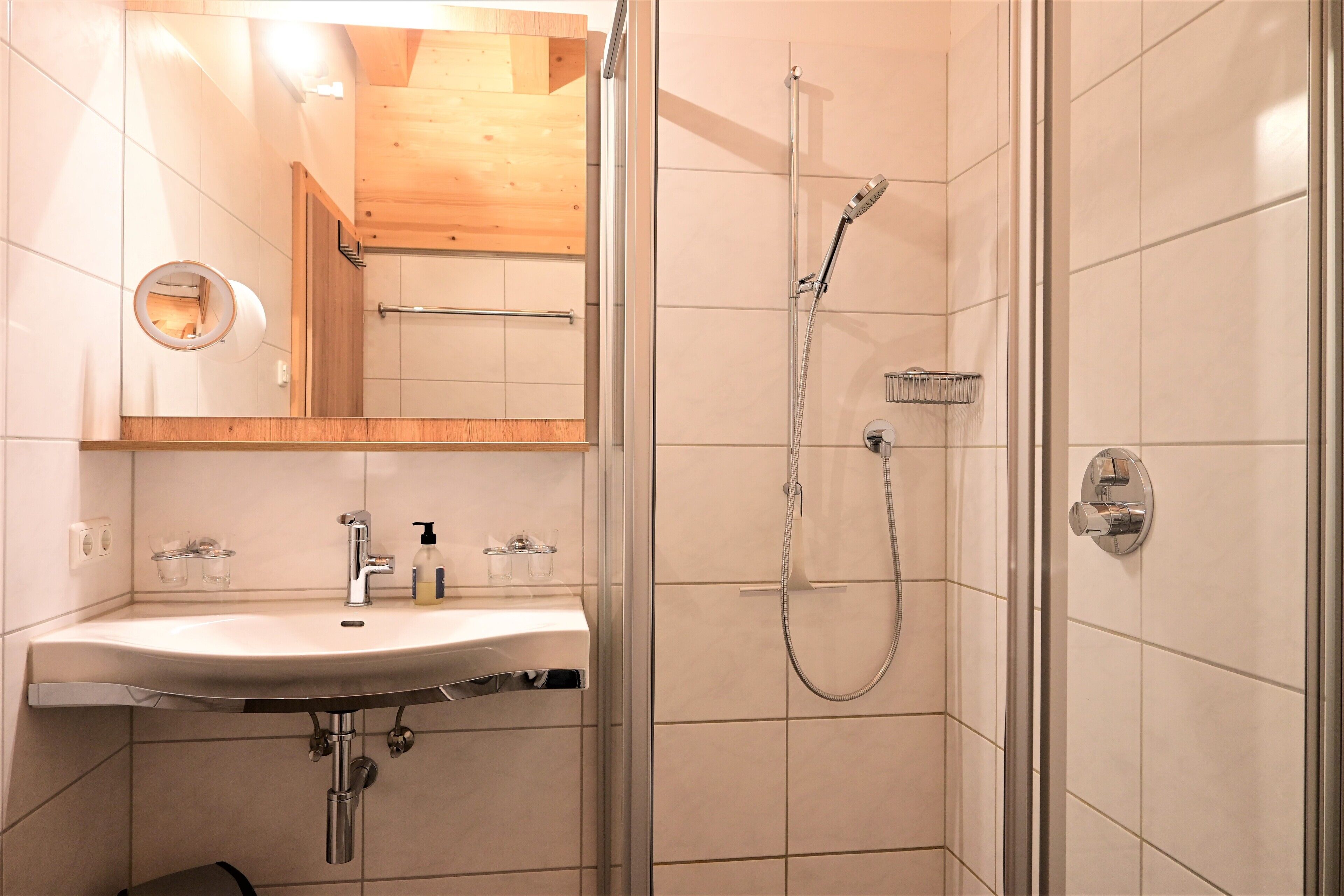 A modern bathroom with a glass-enclosed shower, a sink with a mirror, and a wooden ceiling.