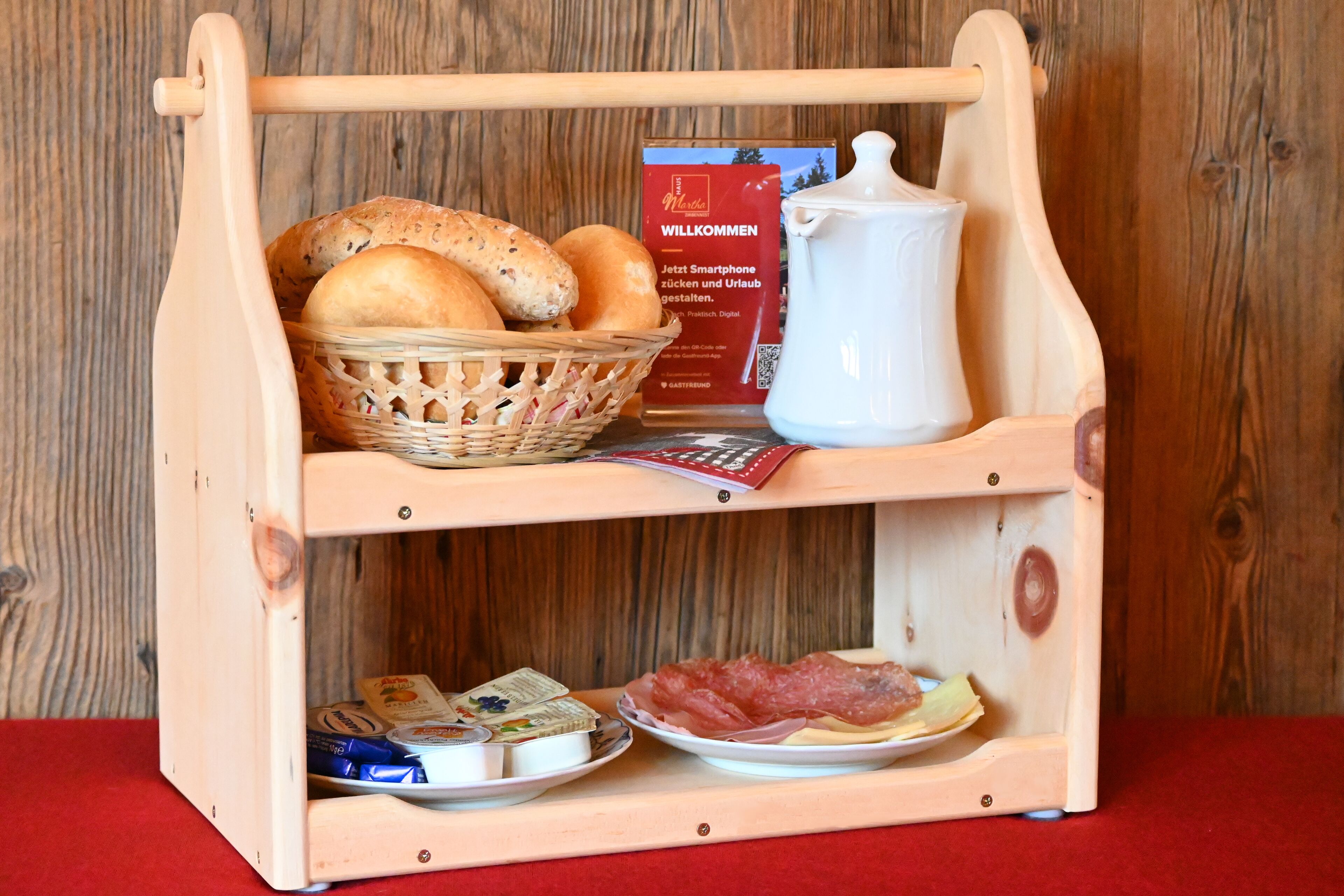 Een houten serveerwagen met brood, een kan en etenswaren.